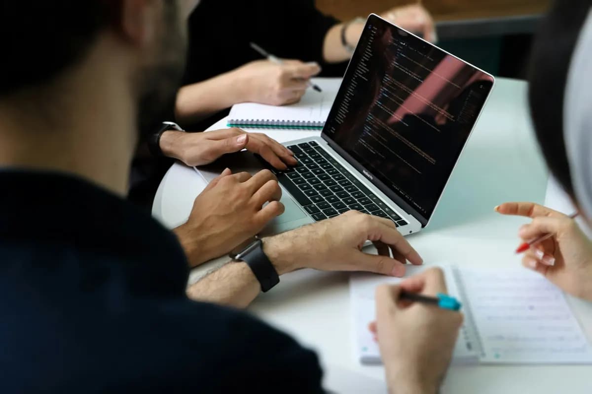 Personas trabajando juntas alrededor de una laptop con código en pantalla
